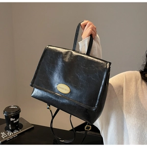 Detail of vintage black oil-wax texture backpack with gold oval metal logo and handle