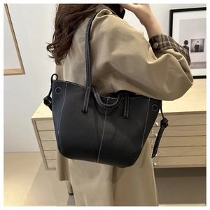 Detail of black pebbled PU leather tote bag with white contrast stitching and side ties
