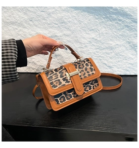 Detail of leopard print canvas bag with brown leather trim and golden metal clasp