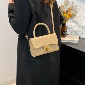 Beige retro tote bag with golden lock and leather strap for women over a black coat