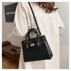 Close-up of a black leather handbag with a gold twist lock worn by a model