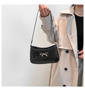 Detail of black crocodile texture shoulder bag with gold bow clasp on beige coat