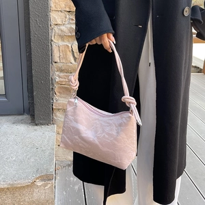 Pink glossy crinkle texture shoulder bag with knot details shown on a model outdoors