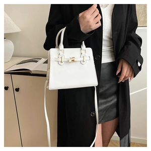 Detail of white leather trapezoid handbag with gold twist lock held by model