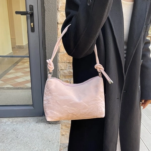 Pink pleated shoulder bag with knotted strap shown on model in black coat