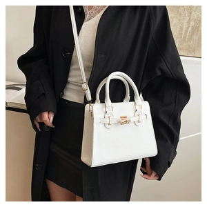 Close-up of white leather handbag featuring metal turn-lock closure and decorative belt strap