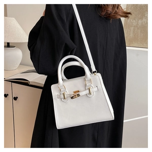 Modern white Kelly-style handbag with golden metal clasp shown on a side table