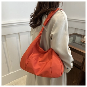 Close-up of orange large capacity hobo tote bag shown on model in modern minimalist setting