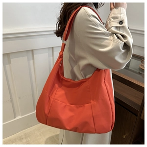 Detail of vibrant orange nylon tote bag showing stitching and wide shoulder strap style