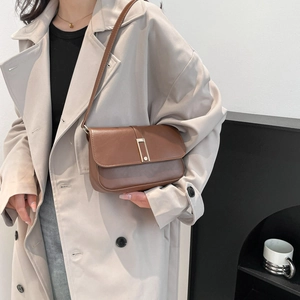Braune Umhängetasche aus Leder mit Goldschnalle am Modell im beigen Trenchcoat