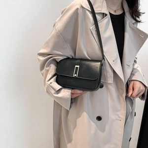 Sac à bandoulière en cuir noir minimaliste avec fermoir doré porté par un mannequin