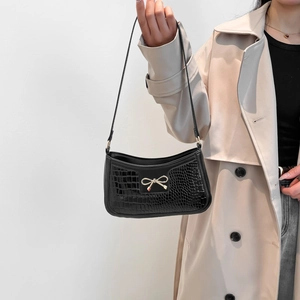 Chic black crocodile embossed shoulder bag with gold bow clasp on a female model