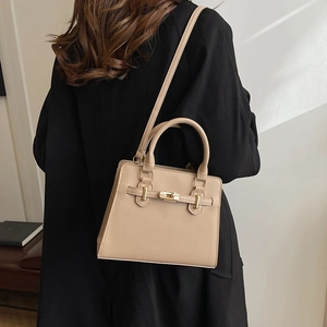 Sac à main chic abricot avec fermoir doré porté sur un élégant manteau noir