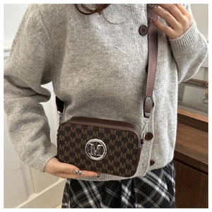 Close-up of retro brown monogram crossbody bag with silver M logo and wide fabric strap