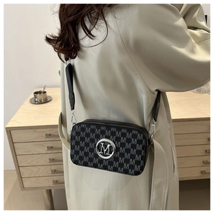 Detail of a black crossbody camera bag with M-pattern print and round metal logo
