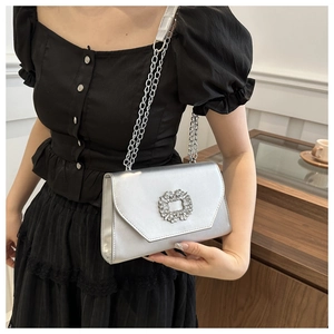 Detail of silver metallic evening bag featuring a crystal-encrusted square buckle and chain