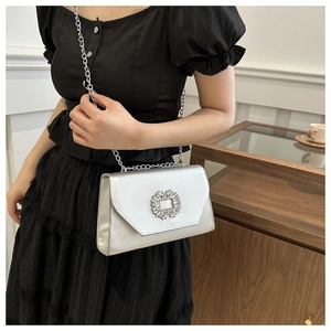 Detailed close-up of a silver clutch with a luxury crystal buckle and metal chain