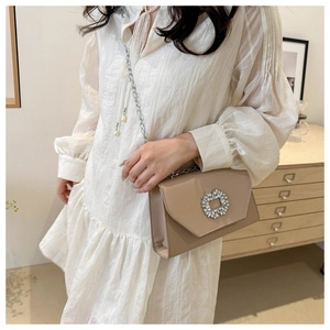 Detail of a beige crossbody square bag with a silver rhinestone buckle and chain strap