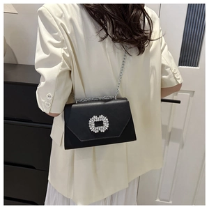 Detail of black leather crossbody bag with sparkling rhinestone buckle on a white blazer