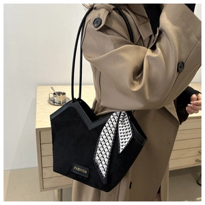 Detail of black suede tote with V-cut edge, gold logo, and decorative silk scarf