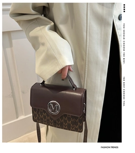 Détail du sac à main marron foncé avec motif M et logo argenté sur trench beige