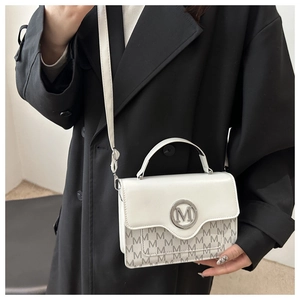 Detail of white and grey monogram shoulder bag worn with a stylish black wool coat