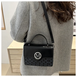 Detail shot of black crossbody bag with silver M logo and monogram on shoulder of model
