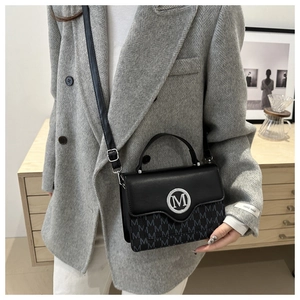 Détail d'un sac à rabat noir avec monogramme 'M' gris et une boucle en métal argenté
