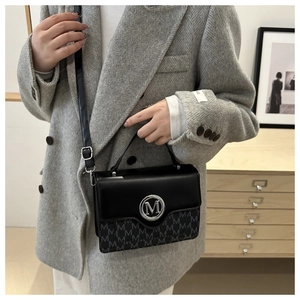 Détail du sac bandoulière noir avec logo M argenté et motif monogramme sur tailleur gris