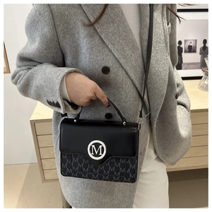 Détail du sac bandoulière noir avec boucle logo M argentée et motif monogramme sur le cuir