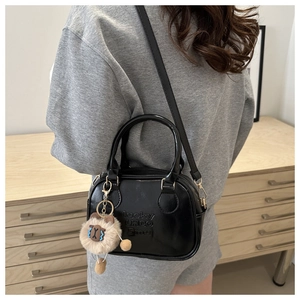 Close-up of black PU leather handbag with a plush bear charm and embossed logo detail