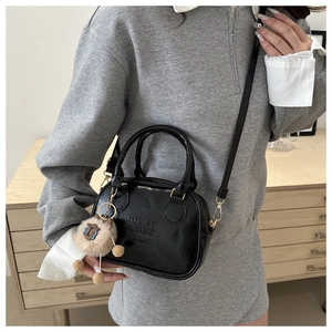 Detail of black mini crossbody bag with embossed text and a cute sheep plush charm