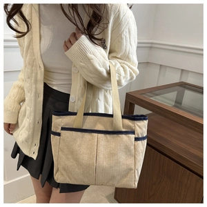 Detail of a beige corduroy tote bag with navy blue trim and front pockets on a model