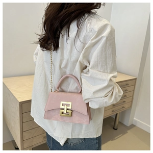 Detail view of light pink crossbody bag with gold geometric clasp and metal chain strap