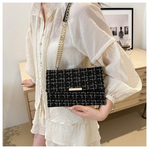 Detailansicht der schwarz-weiß karierten Tweed-Tasche mit Goldkette an einem Model zu Hause