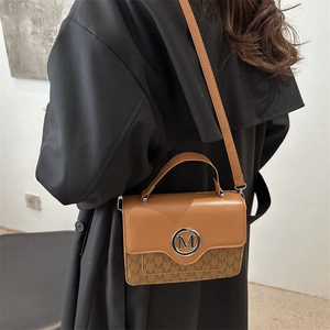 Sac bandoulière marron avec monogramme et logo M en métal dans un cadre mode élégant