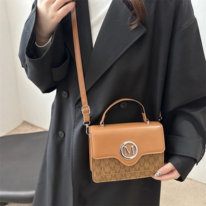 Sac à main élégant en cuir marron avec boucle M argentée et motif monogramme sur un modèle