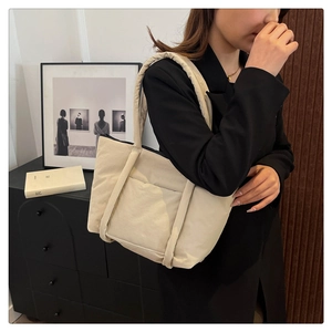 Detail of cream-white quilted tote bag with front pocket shown on a model