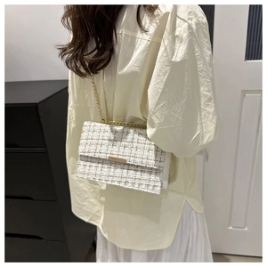 Elegant gestylte beige Tweed-Umhängetasche mit Goldkette an einem weiblichen Model