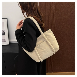Detail of beige quilted puffer tote bag with side pocket shown on shoulder