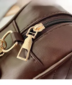 Detail of polished gold-tone metal zipper pull and fine stitching on dark brown leather bag