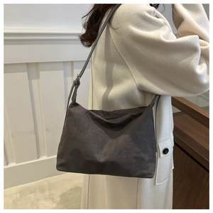 Detail view of large dark grey suede crossbody bag worn over a beige wool coat