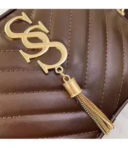 Macro detail of V-quilted brown leather camera bag with gold logo and metal tassel