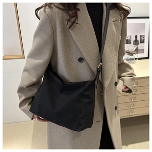 Close-up of a black canvas crescent shoulder bag worn with a stylish wool blazer