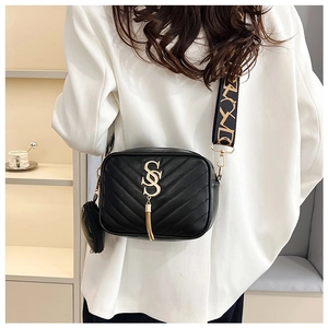 Detail of black quilted crossbody bag with gold logo, tassel, and wide woven strap
