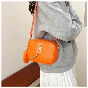 Detail of orange quilted crossbody bag with golden logo, tassel, and mini coin purse