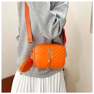 Detail of orange quilted crossbody camera bag with metal logo, tassel, and mini round pouch