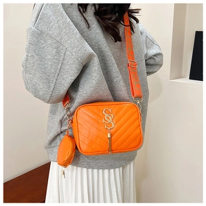 Detail of bright orange crossbody camera bag with V-quilted faux leather and gold tassel
