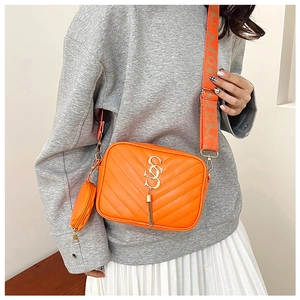 Detail of bright orange crossbody bag with V-quilt pattern, metal logo, and fringe tassel