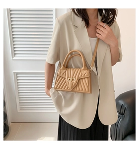 Detailed view of beige quilted handbag featuring a golden turn-lock and arc handle